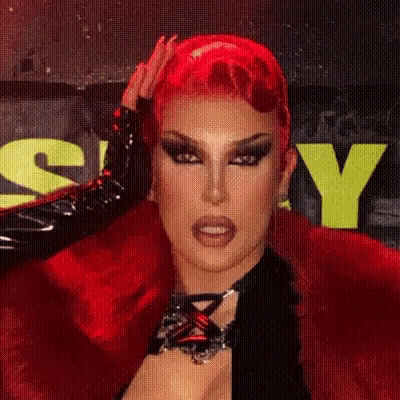 Red-Haired Drag Queen Holding Hair By Yellow Sign GIF