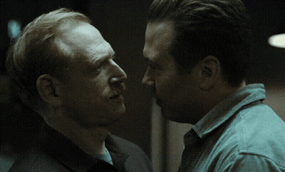 Red-Haired Man With Mustache Talking To Another Man In Dark Room GIF