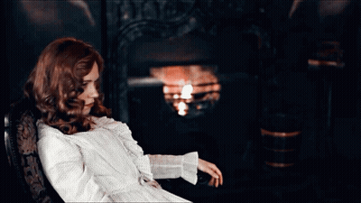 Red-Haired Woman Sitting In Chair By Fire GIF