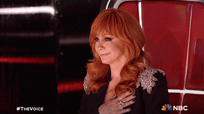 Red-Haired Woman Sitting With Hand on Chest NBC Logo