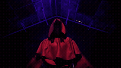 Red Hooded Person Arms Outstretched in Dark Room