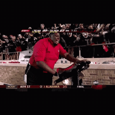 Red Shirt Man Riding Exercise Bike With Masked Crowd GIF