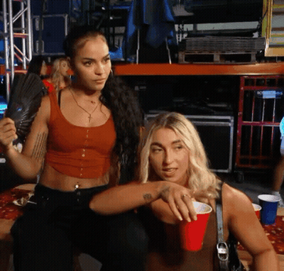 Red Tank Top Woman Holds Fan Near Blonde With Red Cup GIF