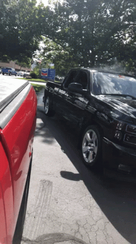 Red Truck Parked Next To Black Truck In Front Of Chevron Sign GIF