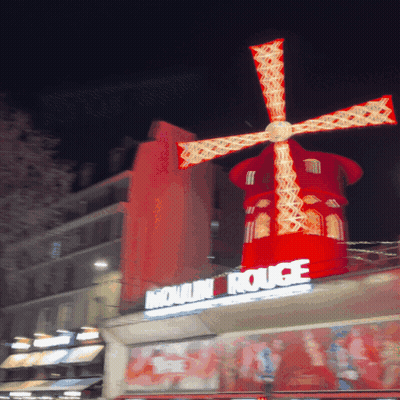Red Windmill Lit Up In Front Of Moulin Rouge Sign GIF