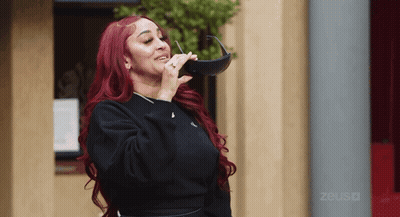 Redhead Woman Holding Sunglasses In Front Of Zeus Building GIF