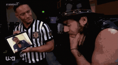 Referee Shows Wrestler Picture, Other Wrestler Looks Down GIF