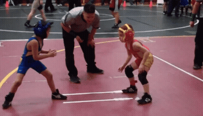 Referee Watching Two Boys Wrestle On Red Mat GIF