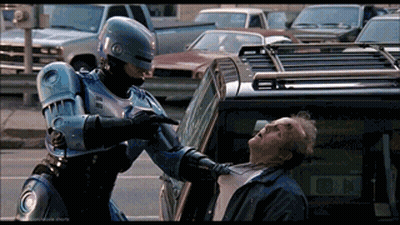 Robot Pointing Gun At Man In Front Of Car With Letter N GIF