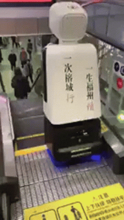 Robot Sitting On Escalator With Chinese Writing GIF
