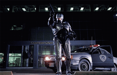Robot Standing In Front Of Contemporar Building GIF