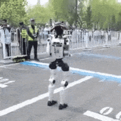 Robot Walking In Parking Lot As People Watch GIF