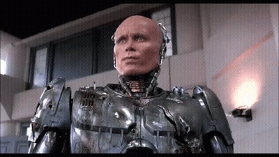 Robot With Bald Head Standing In Room With Wall Light GIF