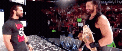 Roman Reigns And Seth Rollins Are Standing Next To Each Other On A Stage . GIF