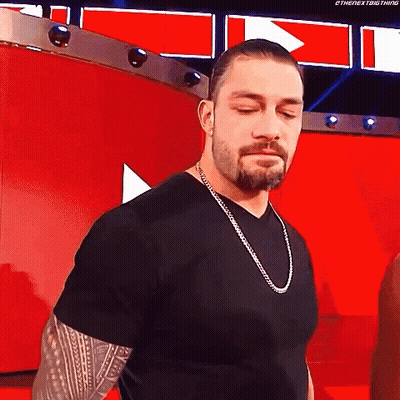 Roman Reigns Is Wearing A Black T-Shirt And A Silver Chain Around His Neck . GIF