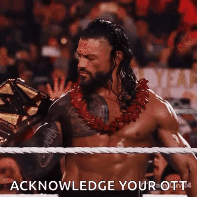 Roman Reigns Is Wearing A Lei And Holding A Wrestling Championship Belt In A Wrestling Ring . GIF