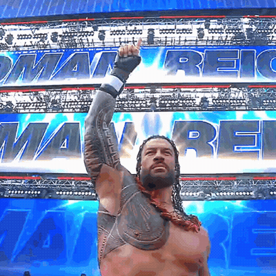 Roman Reigns Raises His Fist In The Air In Front Of A Banner That Says ' Roman Reigns ' GIF