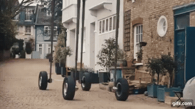 Row Of Houses On Cobblestone Street With Large Wheels GIF