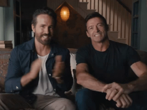Ryan Reynolds And Hugh Jackman Are Sitting On A Couch And Smiling GIF