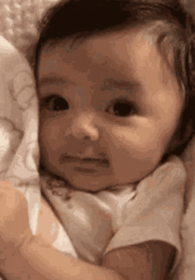 Sad Baby Lying In Blanket Looking At Camera GIF