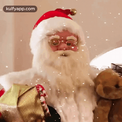 Santa Claus Is Holding A Teddy Bear And A Gift Box While Snow Falls Around Him . GIF