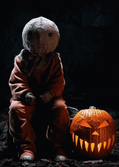 Scarecrow Sitting Next To Carved Pumpkin In Dark GIF