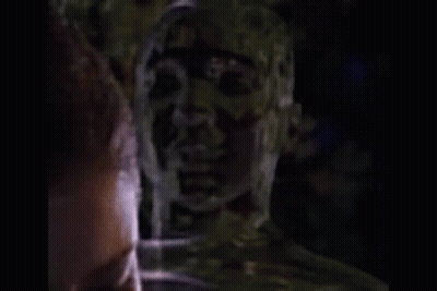 Shaved Head Man Talking To Another In Dark GIF
