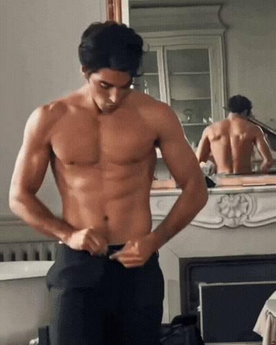 Shirtless Man Adjusting Pants By Fireplace GIF