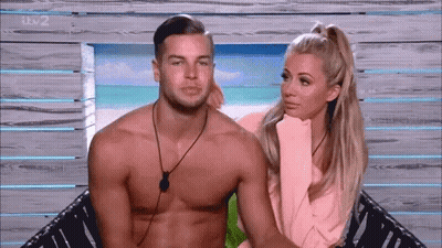 Shirtless Man And Woman Sitting On Beach GIF