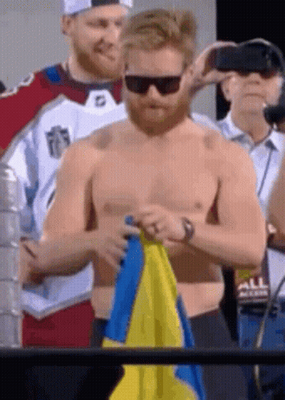 Shirtless Man Holding Blue And Yellow Flag GIF