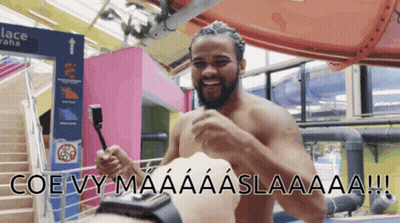 Shirtless Man Holding Remote In Front Of Lace Sign GIF