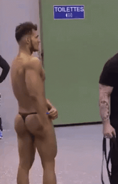 Shirtless Man In Thong In Front Of Blue Toilettes Sign GIF