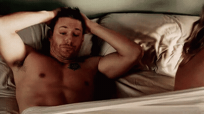 Shirtless Man Laying In Bed With Woman Standing Next To Him GIF