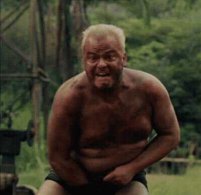 Shirtless Man Sitting In Field With Hands On Stomach GIF