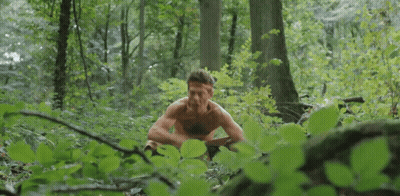 Shirtless Man Sitting In Woods Eating Leaf GIF