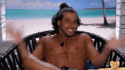 Shirtless Man Sitting On Beach With Arms Outstretched GIF