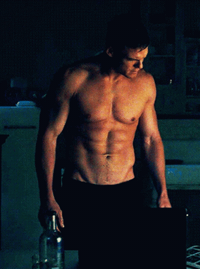 Shirtless Man Standing Hands On Hips In Dark Room GIF
