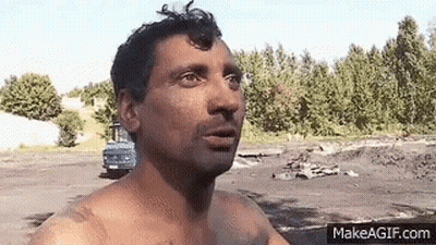 Shirtless Man Standing In Field With Blue Truck GIF