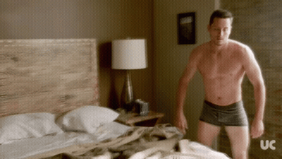 Shirtless Man Standing in Front of Bed With UC