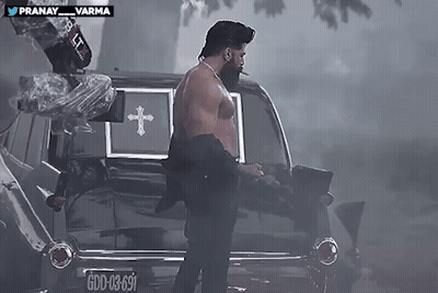 Shirtless Man Standing In Front Of Black Coffin With Cross GIF