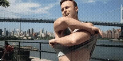 Shirtless Man Taking Off Shirt In Front Of Bridge GIF