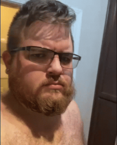 Shirtless Man With Beard And Glasses Taking Selfie In Bathroom GIF