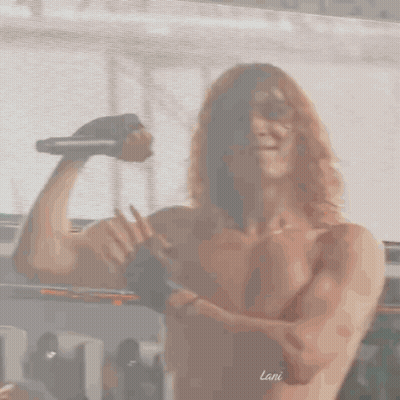 Shirtless Man With Curly Hair Holding Microphone Flexing GIF