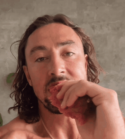 Shirtless Man With Long Hair Eating Meat GIF