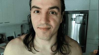 Shirtless Man With Long Hair Smiling in Front of Refrigerator
