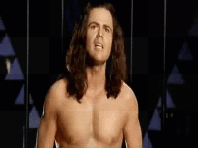 Shirtless Man With Long Hair Standing In Front Of Triangle Wall GIF