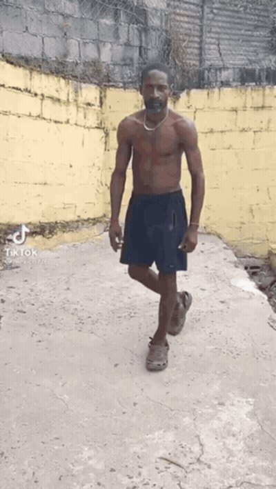 Shirtless Man With Mustache and Necklace Walking Down Sidewalk