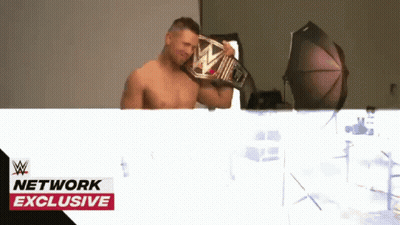 Shirtless Wrestler Holding Wrestling Belt In Front Of Network Exclusive Banner GIF