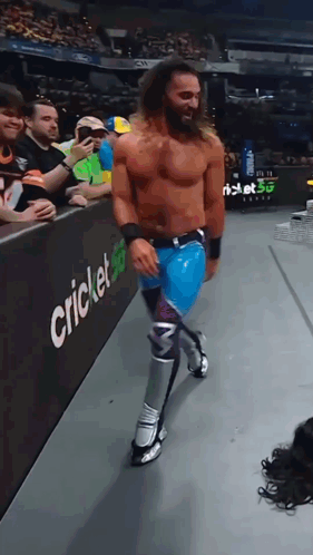Shirtless Wrestler Walking Past Cricket Sign GIF