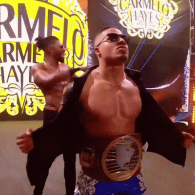 Shirtless Wrestler With Belt In Front Of Carmelo Hayes Sign GIF